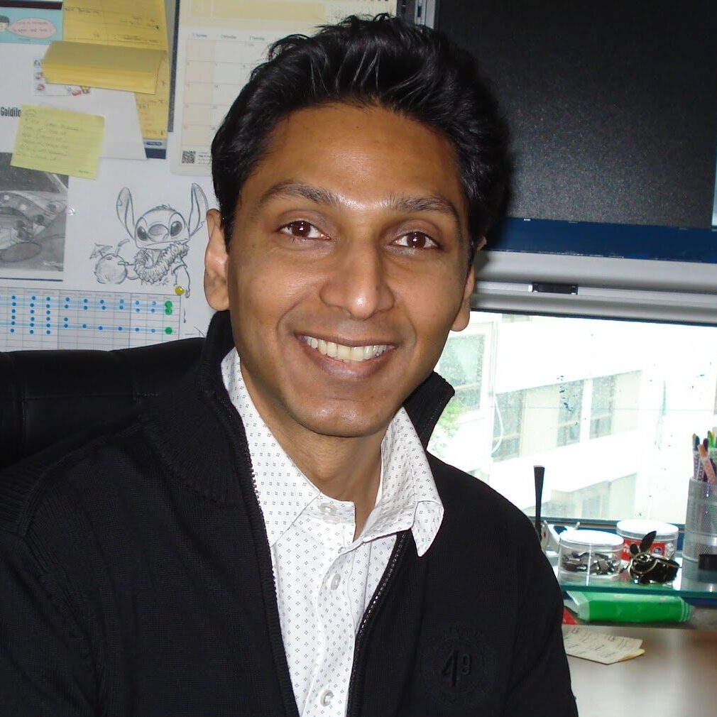 Man smiling at the camera, a computer and desk behind him.